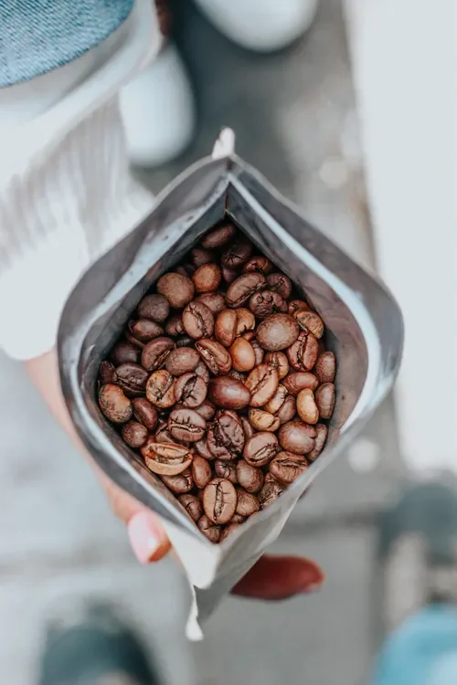 A hand holding an open bag of roasted coffee beans