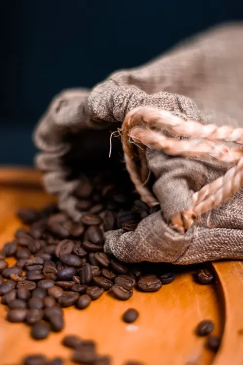 Roasted coffee beans spilling from a burlap sack onto a tray