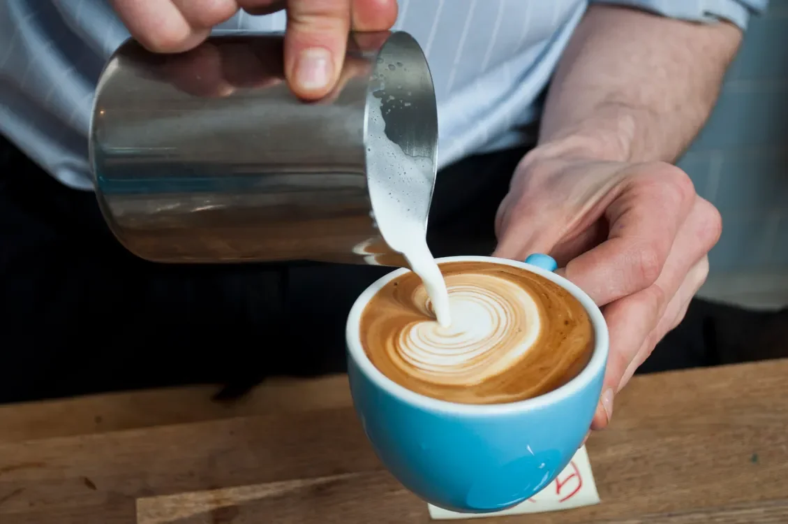 A barista pouring milk into a blue cup to make latte art