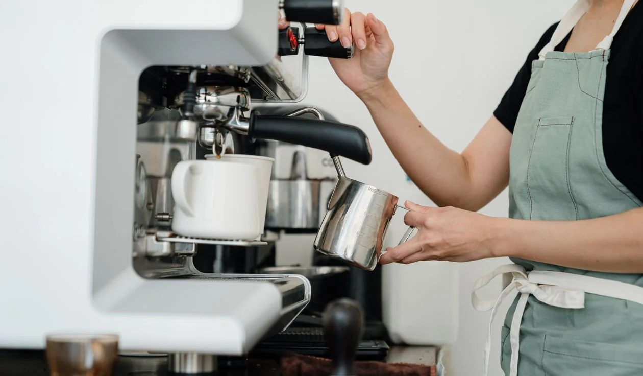 A barista steaming milk with a pitcher at an espresso machine