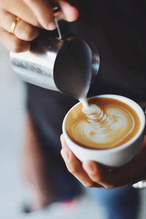 A barista pouring milk to make latte art